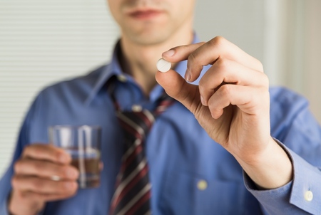 Close-up view photo of female hands holding one white round pill and glass of water. Young woman taking medication, feeling ill. Healthcare conceptの写真素材