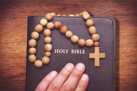 Mans hand on the old bible with rosary beads on the brown table in the quiet, dark atmosphere....