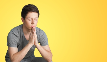 Young man praying against yellow background
