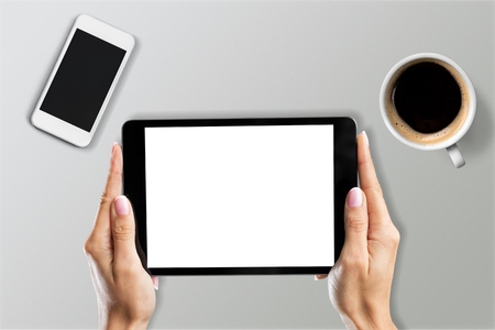 Young man hands holding digital tablet on wooden table with phone i cup of coffeeの写真素材