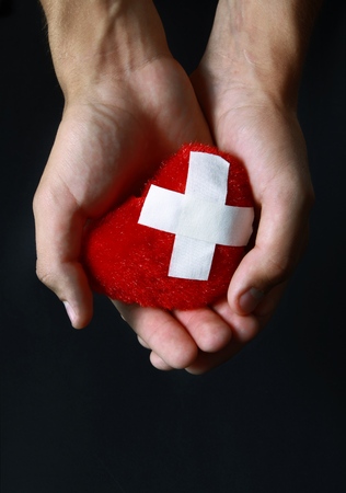 Man Holding Toy Heart with Adhesive Bandage - on Black Backgroundの写真素材