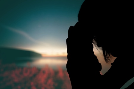 Young woman praying  on sunset background