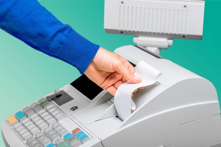 Cash register with LCD display and workers hand holding receipt paper over blurred supermarket interorの写真素材
