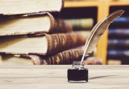 Quill pen and ink well resting on an old book in a library concept for literature, writing, author and historyの写真素材