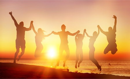 Friends jumping on beach at seaside at sunsetの写真素材