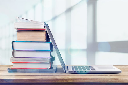 Stack of books with laptop on wooden table