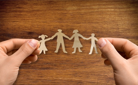 Paper family in hands on wooden coloured background welfare conceptの写真素材