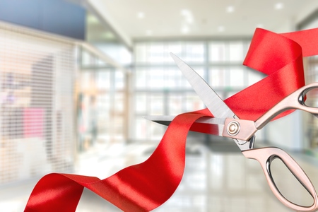 Scissors cutting red ribbon, close-up view on blue backgroundの写真素材