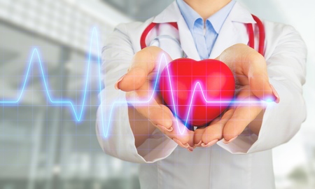Female medical doctor holding red heart shape in hand with graphic of heart beat, cardiology and insurance conceptの写真素材