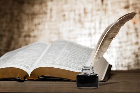 Quill pen and ink well resting on an old book in a library concept for literature, writing, author and historyの写真素材