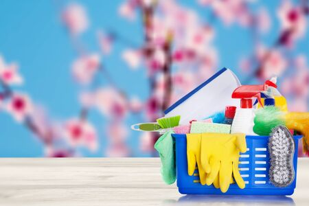Bucket or basket with cleaning items on wooden table and blurry pink flowers tree background. Washing set with copy space banner.の写真素材