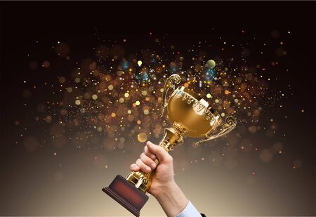Man holding up a gold trophy cup with abstract shiny background, copy space for textの写真素材