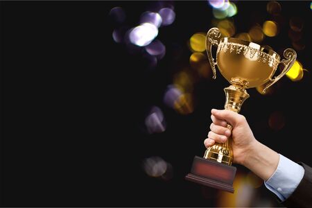 Close-up human hand holding golden Trophy on blurred  backgroundの写真素材