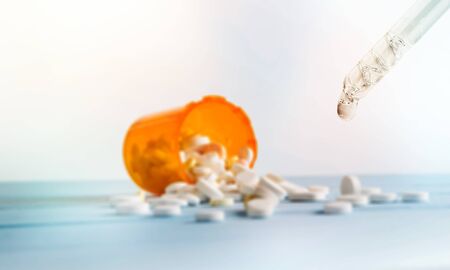 Hemp CBD oil capsules spilled from a bottle and CBD tincture dripping from a glass dropper onto a...