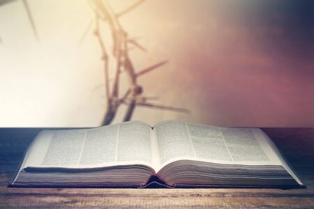 Open Bible with a light coming from above on a wooden desk and a Crown of Thorns in the wall.