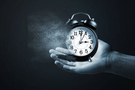 Concept of passing away, the clock breaks down into pieces. Hand holding analog clock with dispersion effectの写真素材