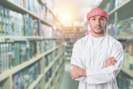 Arab student standing in library holding books on his arms. education concept.