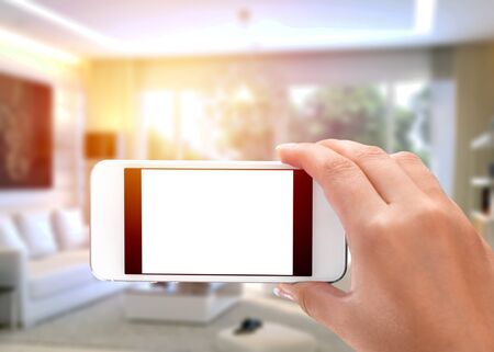 Man hand holding the black smartphone with big blank screen and modern frame less design in home interior, living room - isolated on white background angled positionの写真素材