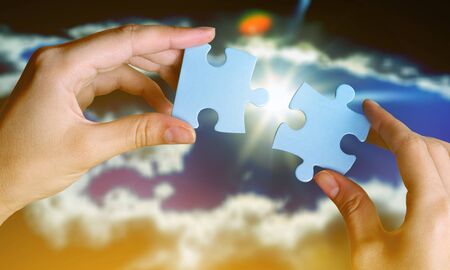 two hands trying to connect couple puzzle piece with sunset background. Jigsaw alone wooden puzzle...