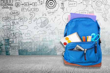 Open blue school backpack on wooden table in classroom background.