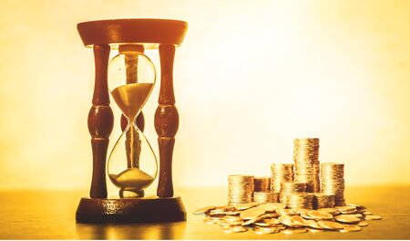 Sand running through the shape of hourglass on table with banknotes and coins of international...