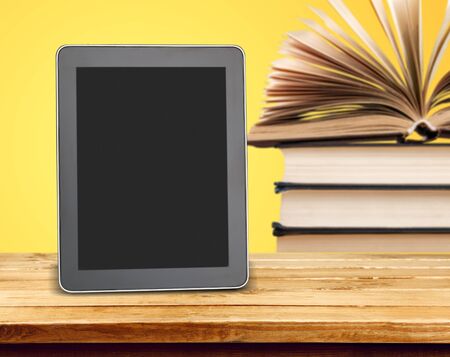 Stack of books versus kindle or tablet for reading, technology innovative education concept on yellow background, copy spaceの写真素材