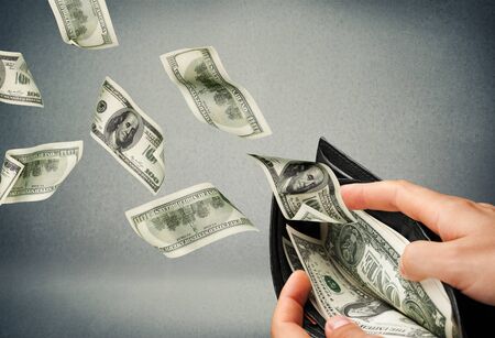 Sad man looking at his wallet with money dollar banknotes flying out awayの写真素材