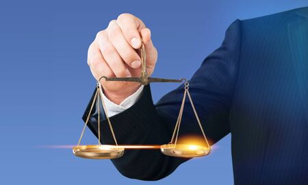 Close-up business man holding scales in hand on blurred gray background
