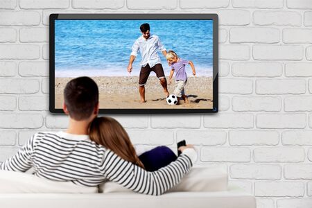 Young happy loving couple sitting on sofa indoors and watching TV.