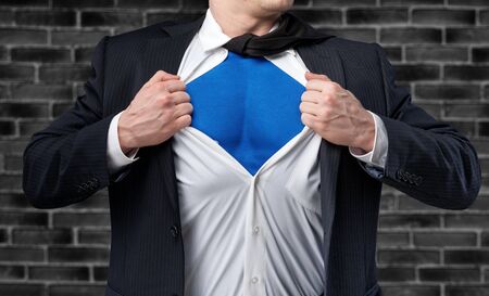 Businessman tears shirt on himself to show that he is Superhero isolated on white backgroundの写真素材