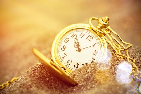 Gold pocket watch in the sand in the sunsetの写真素材