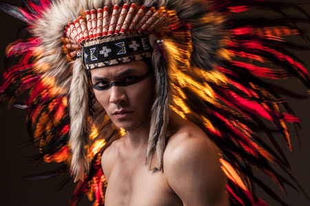 Naked indian man with traditional native american make up and headdress looking at the camera. Mixed light studio shotの写真素材