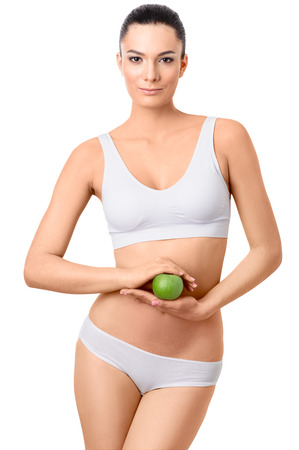 Woman in underwear with beautiful slim body posing with green apple on the white background. Eco, bodycare, healthcare conceptの写真素材