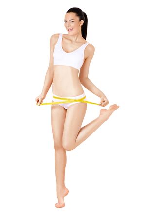 Slim full-lenght woman in white underwear and measure around her body on white background isolated. Healthcare, diet, weight loss and body care conceptの写真素材