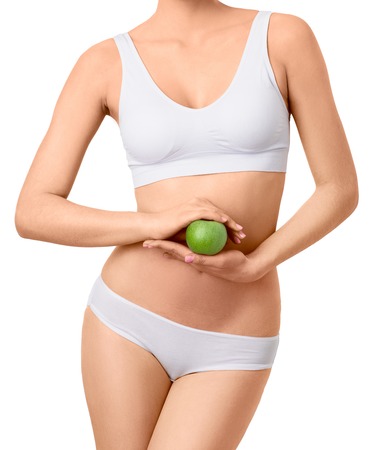 Slim woman in white underwear with green apple at her hands over isolated background. Bodycare, healthcare, diet concept without faceの写真素材