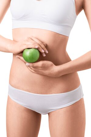 Slim woman in white underwear with green apple at her hands over isolated background. Bodycare, healthcare, diet concept without faceの写真素材