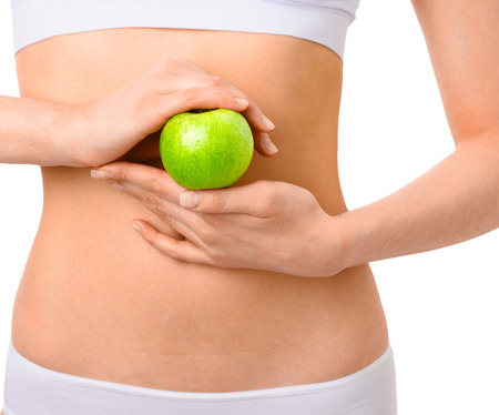 Slim woman in white underwear with green apple at her hands over isolated background. Bodycare, healthcare, diet concept without faceの写真素材
