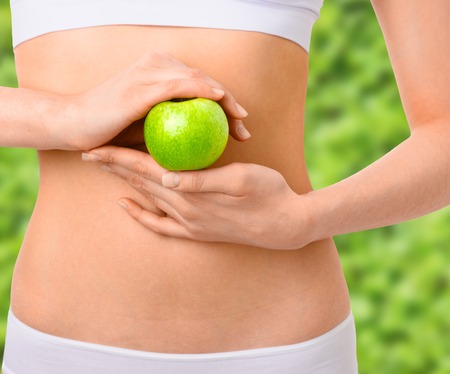 Slim woman in white underwear with green apple at her hands over isolated background. Bodycare, healthcare, diet concept without faceの写真素材