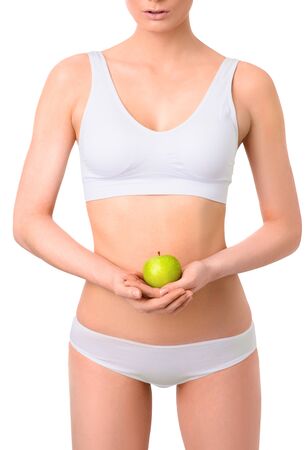 Slim woman in white underwear with green apple at her hands over isolated background. Bodycare, healthcare, diet concept without faceの写真素材