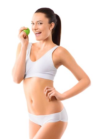 Happy slim woman in white underwear posing with green apple at her hands over isolated background. Bodycare, healthcare, diet concept without faceの写真素材