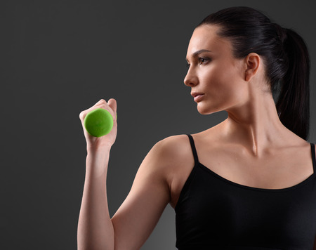 Fitness woman working out with green dumbbell looking at the side on dark background. Fitness conceptの写真素材