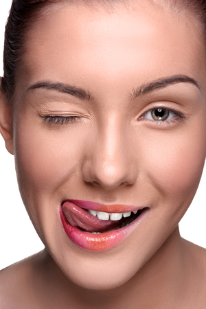 Close up head shot. Young woman with colorful lips make up showing her tongue  on isolated white background. Lok at the cameraの写真素材