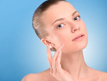 Woman applying lifting cream on face, over blue backgroundの写真素材