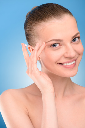 Woman applying lifting cream on face, over blue backgroundの写真素材