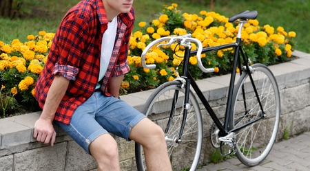Hipster man with bicycle resting over flowerbed withal yellow flowers. WIthout face. Side viewの写真素材