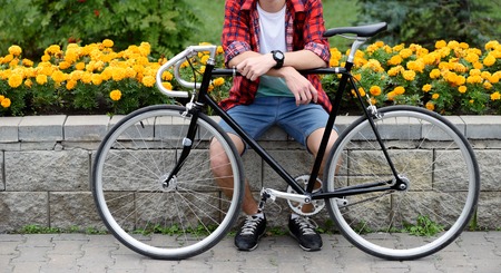 Hipster man with bicycle resting over flowerbed withal yellow flowers. Without face. Front viewの写真素材