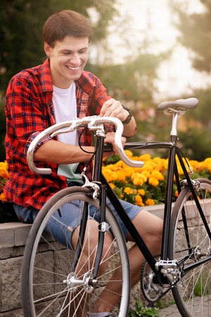 Handsome, happy man with his bicycle Sitting on flowerbed withal yellow flowersの写真素材