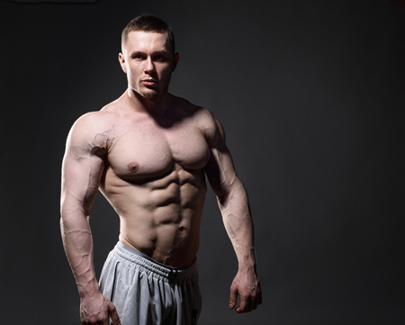 Bodybuilder in studio over dark background shows his muscle.の写真素材