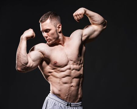 Bodybuilder in studio over dark background shows his muscles.の写真素材