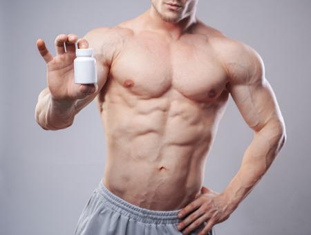Bodybuilder with a white jar of pills on neitral background. Studio Shot without faceの写真素材
